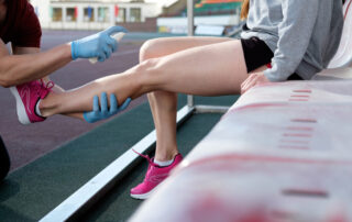 A coach spraying analgesic spray on a female runner's leg