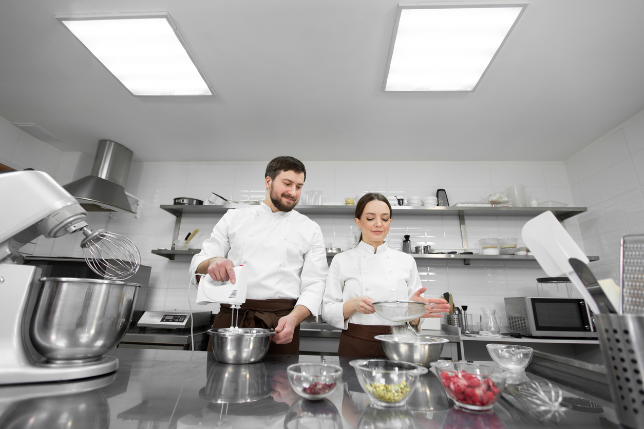 Pastry chef a man and a woman in a professional kitchen prepare a sponge cake.